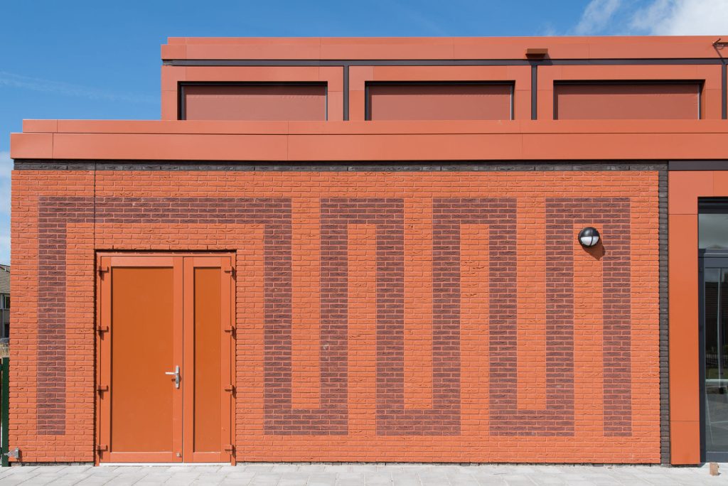 Rode gevel met tekening in het metselwerk en een rode deur