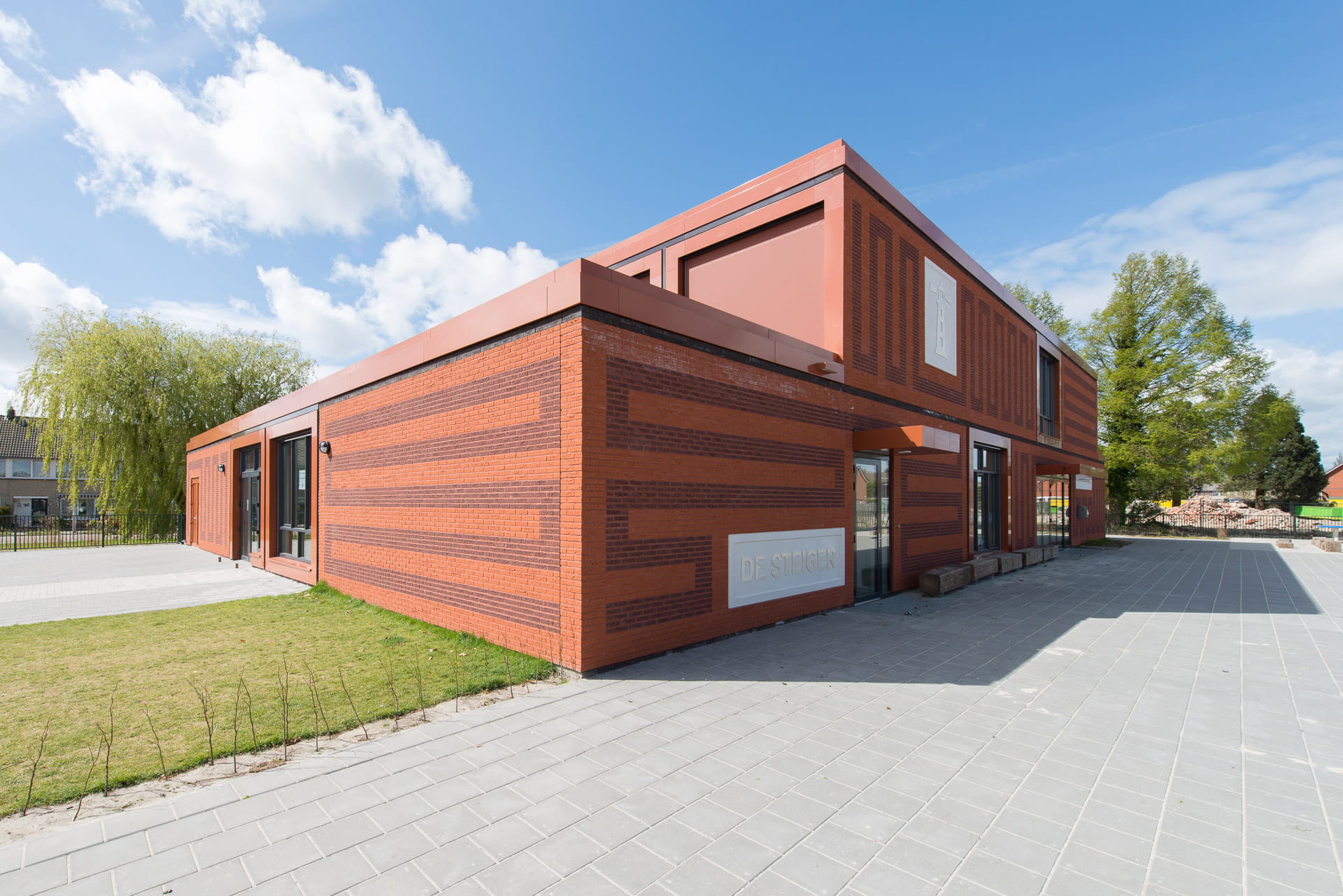 Hoek van MFA Lemstervaart, een rood gebouw met rode voeg en tekeningen in het metselwerk en op de voorgrond een plein