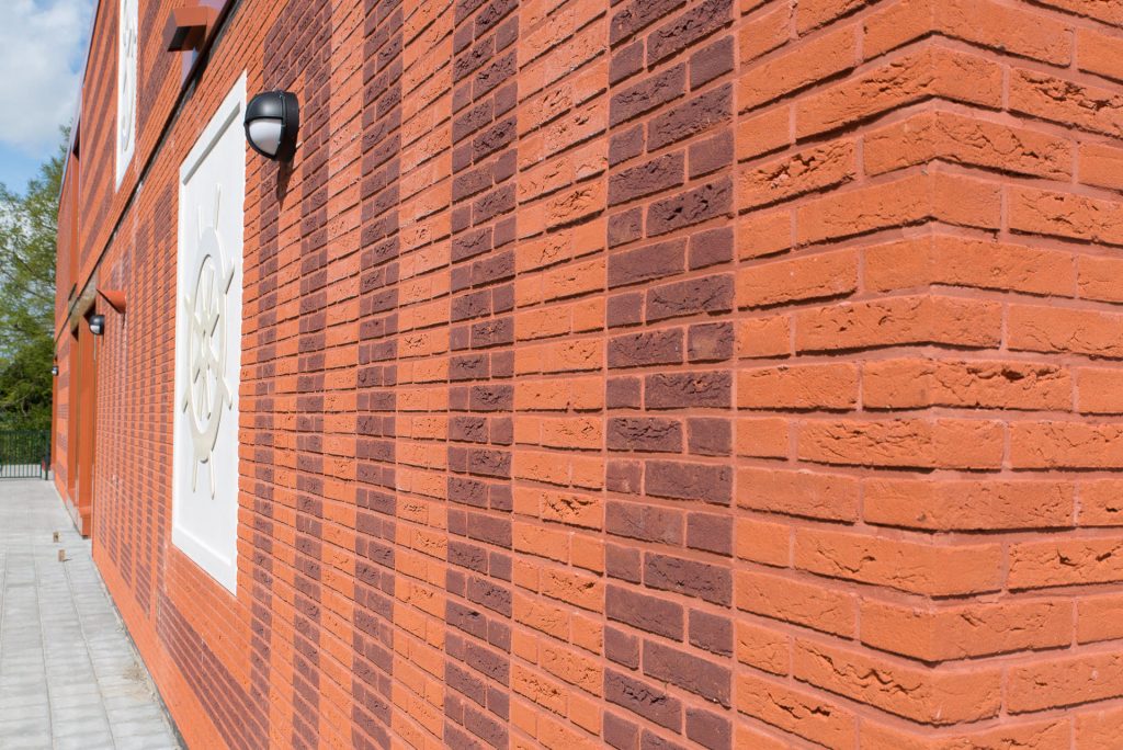 Hoek van muur met rode bakstenen en tekening van donkere stenen erin