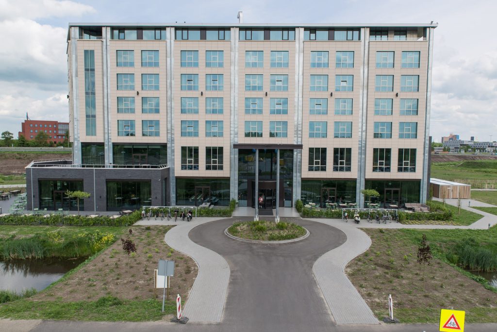 Voorzijde van het Van der Valk met lichte tegels, veel ramen en donker metselwerk onderaan