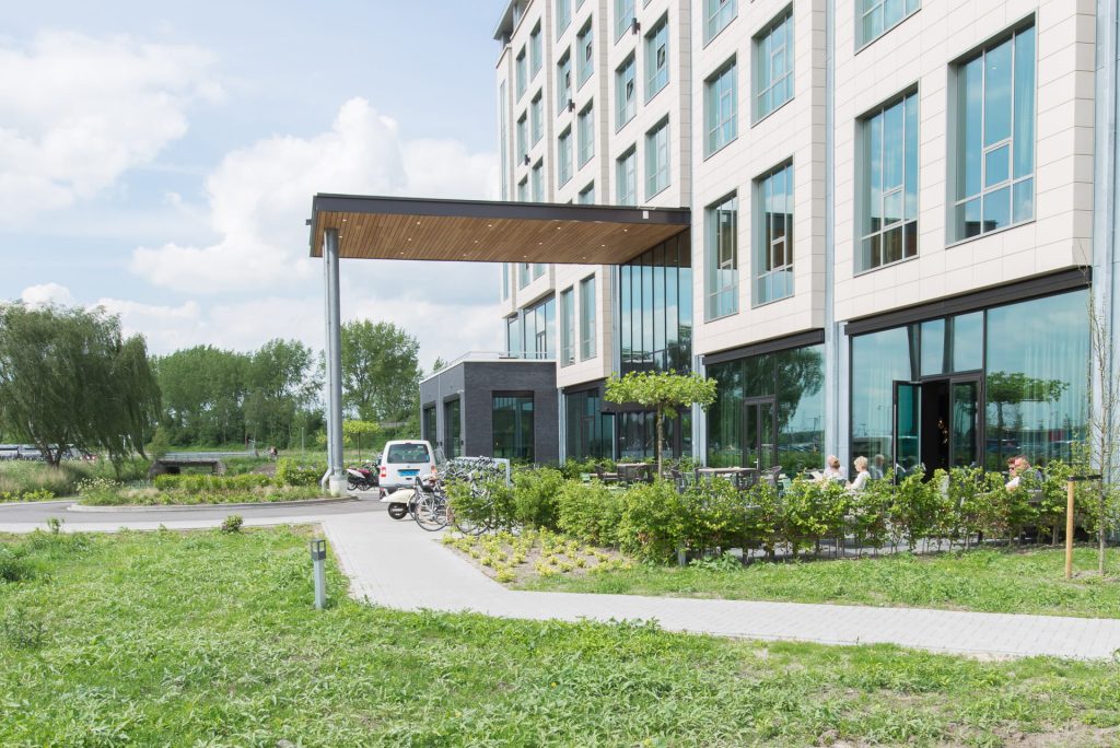 Witte gevel van het Van der VAlk hotel met een afdak ervoor en een rotonde en een horecagelegenheid