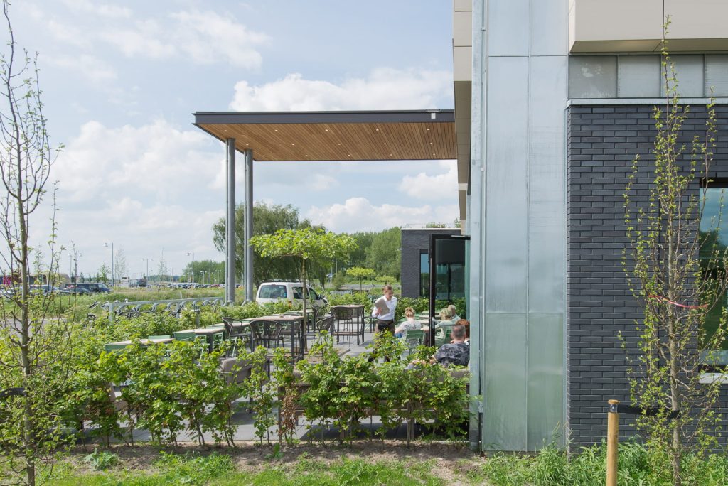 Zijkant van een gevel met een terras waar mensen in de zon zitten