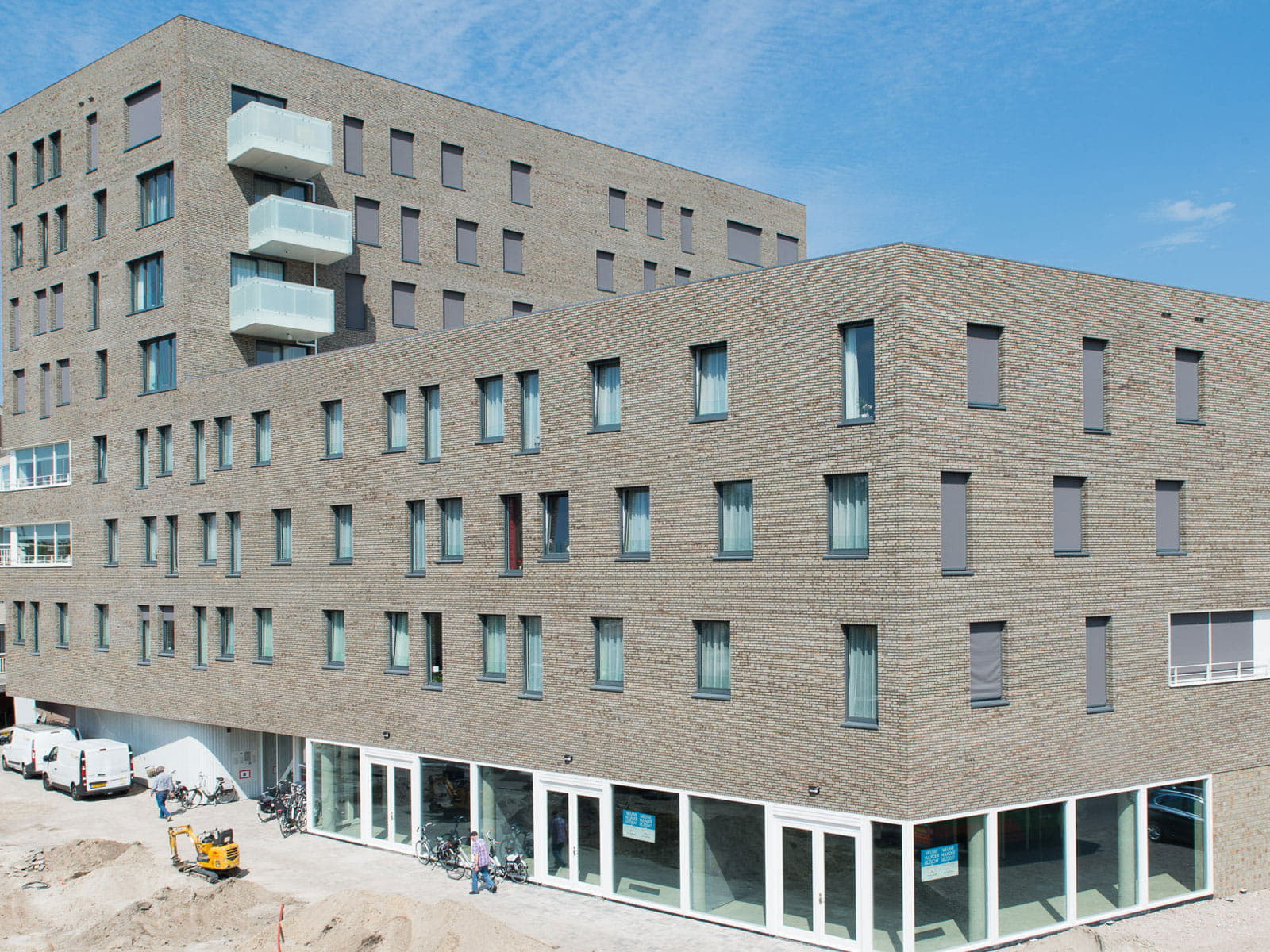 Zijaanzicht van hoogbouw in een bruingrijze steen met veel ramen tegen een blauwe lucht