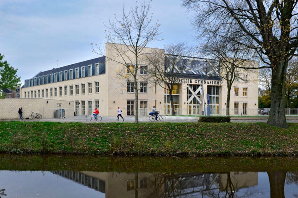 Schoolgebouw op de achtergrond en kinderen op de fiets met op de voorgrond een gracht