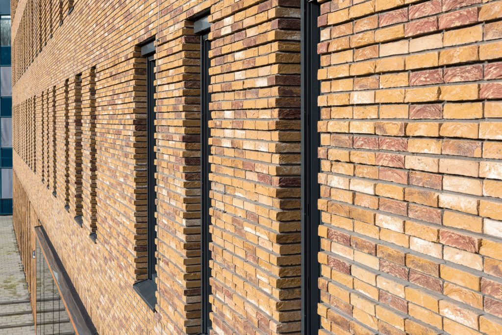 Muur met lichtgele bakstenen en uitstekend metselwerk tussen ramen