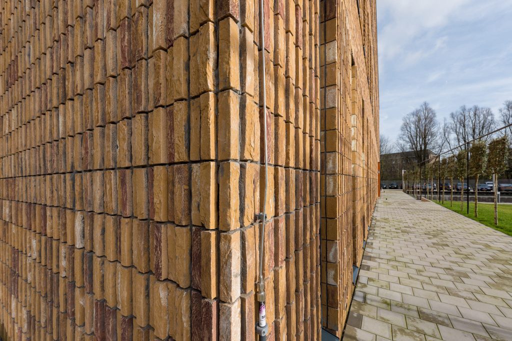 Hoek van een gevel met ruige gelige steen die staand gemetseld is