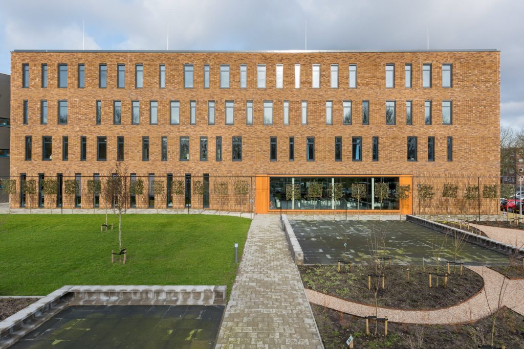 Vooraanzicht van Hoornbeeck College Rotterdam met ramen en vlakken, oranje element in de gevel en tuin op de voorgrond