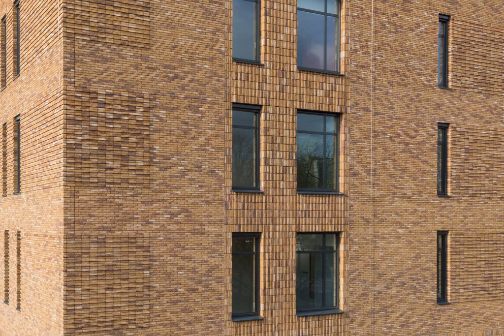 Verschillende type metselwerk op een gele gevel met zwarte ramen