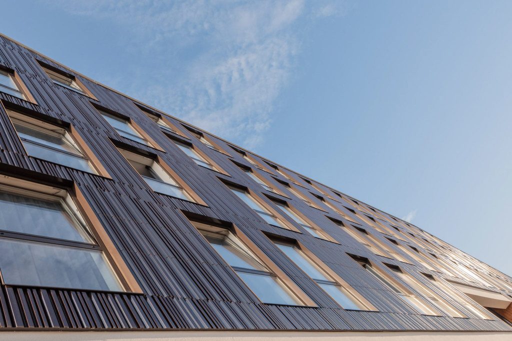 Detail van een gevel met ramen, van onderen genomen. De tegels zijn bruinig met een patroon, tegen een blauwe lucht