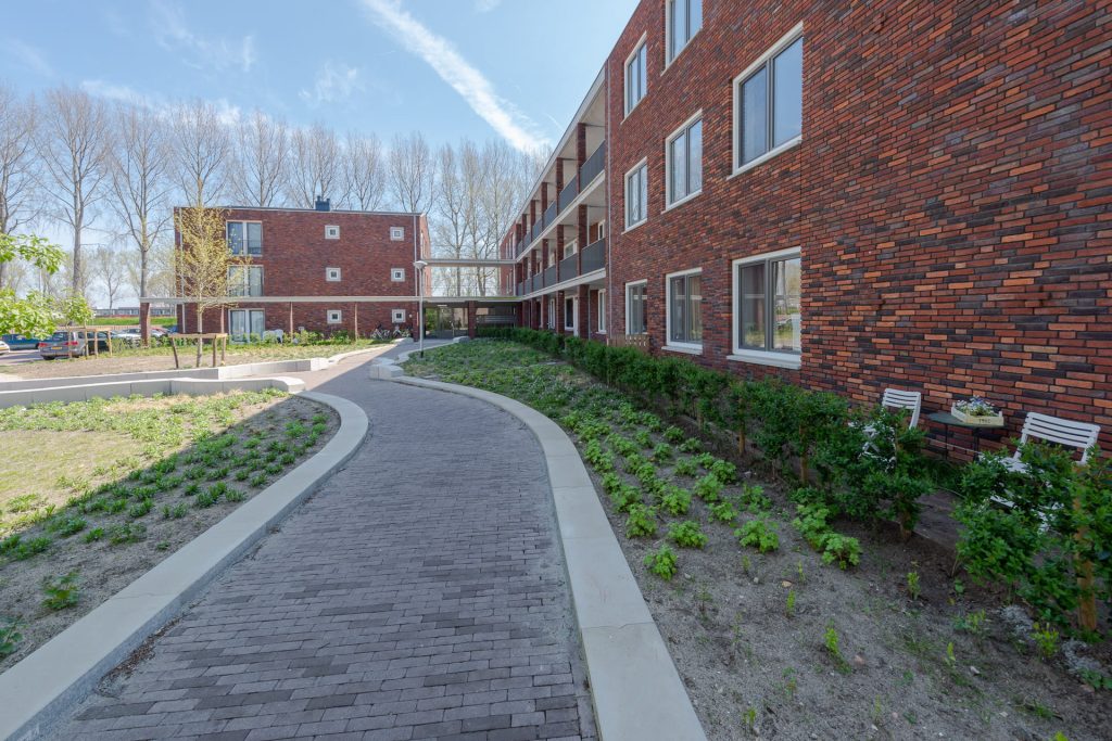 Roodbruin gebouw naast een slingerend pad met op de achtergrond nog een gebouw en bomen