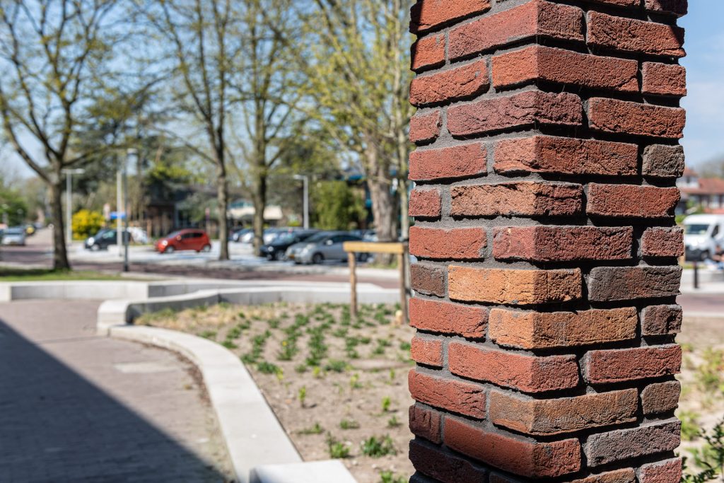 Pilaar van roodbruine steen met op de achtergrond staat en bomen