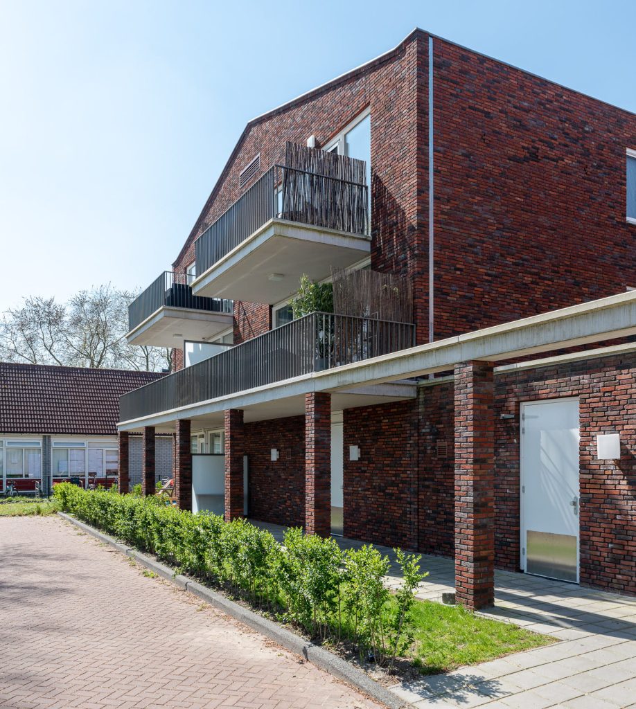 roodbruin gebouw met een balkonrij en groenstrook ervoor