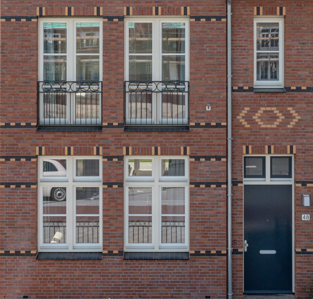 Close-up van een gevel met vier ramen en een deur in een rode steen