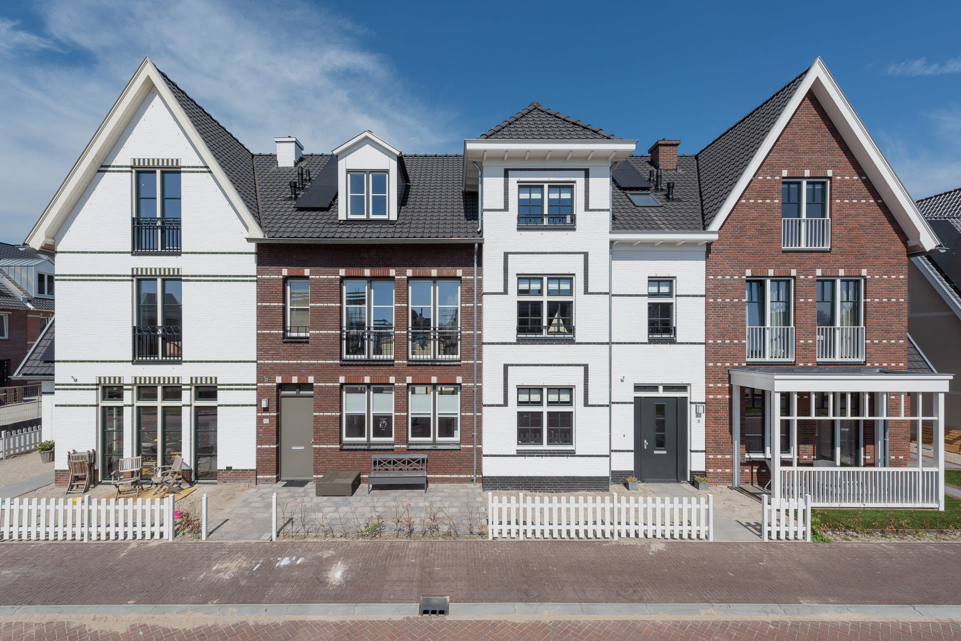 Rij van vier woningen in eind negentiende eeuwse stijl, maar nieuwgebouwd in verschillende kleuren wit en rood/bruin