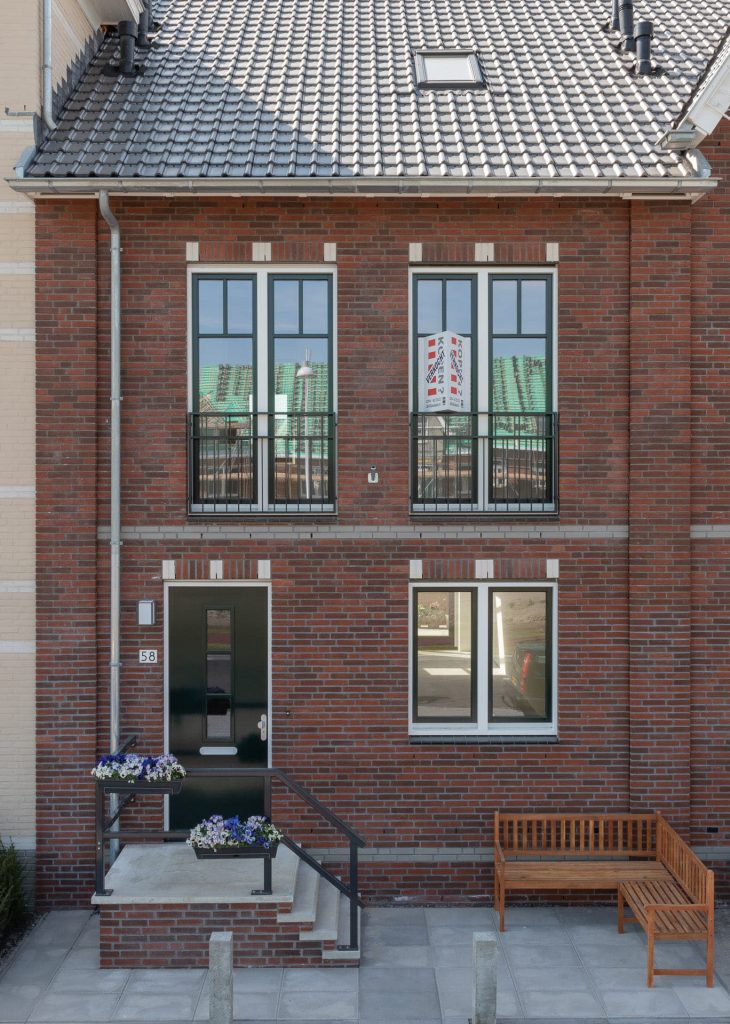 Gevel van rode steen met een voordeur met een trapje en drie ramen