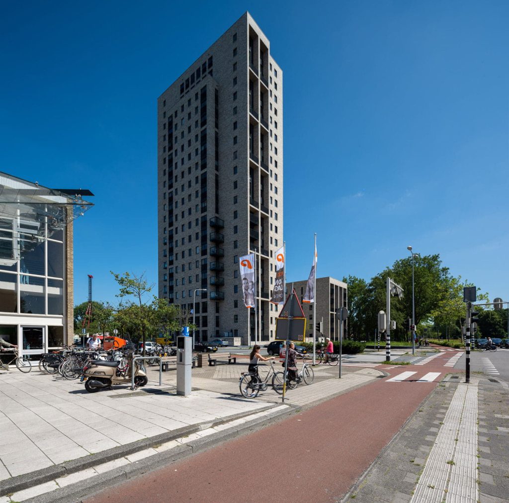 hoge toren met lichte gevelstenen en steentrips met op de voorgrond een fietspad en verkeer