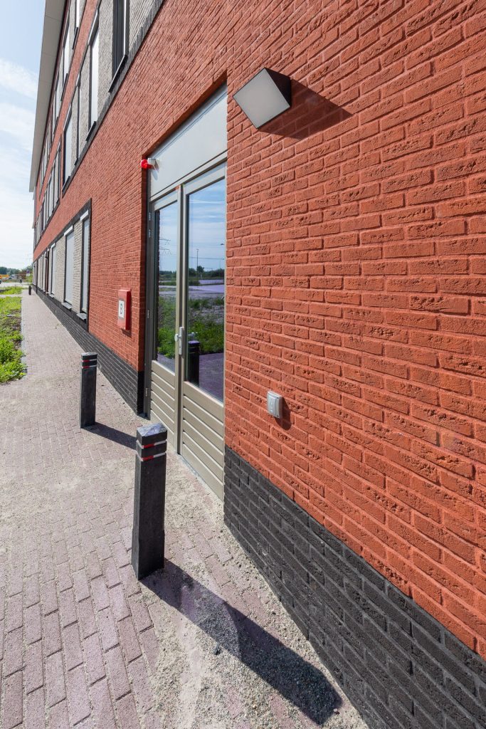 Zijkant van een rode gevel met een deur en paaltjes ervoor