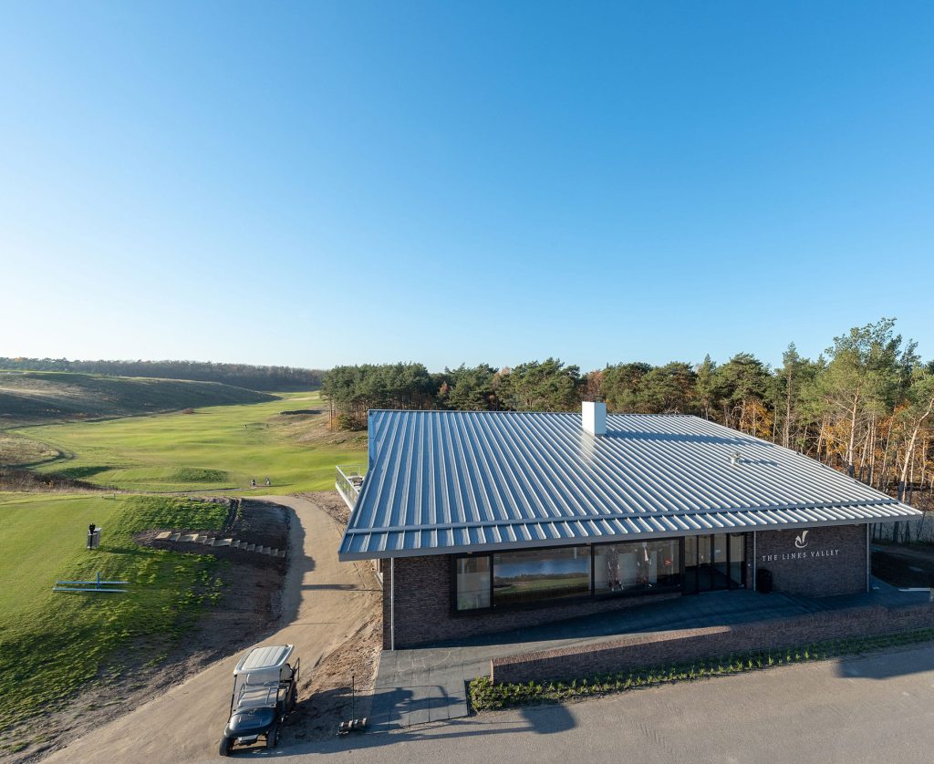 Zicht op een golfbaan met op de voorgrond een gebouw met een schuin dak
