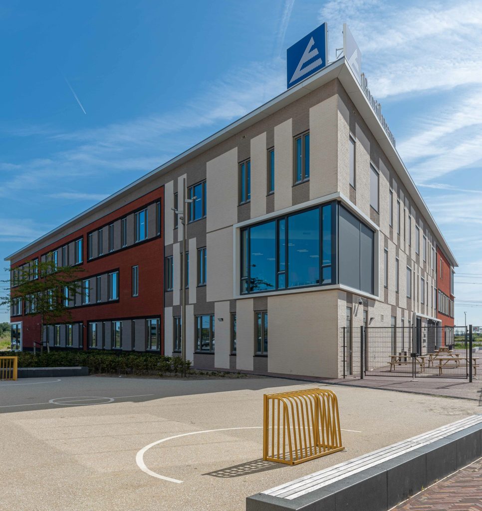Gevel met lichte en rode stenen met op de voorgrond een schoolplein