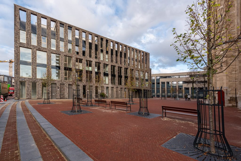 Zijkant van lichte gevel met grote ramen en plein op de voorgrond