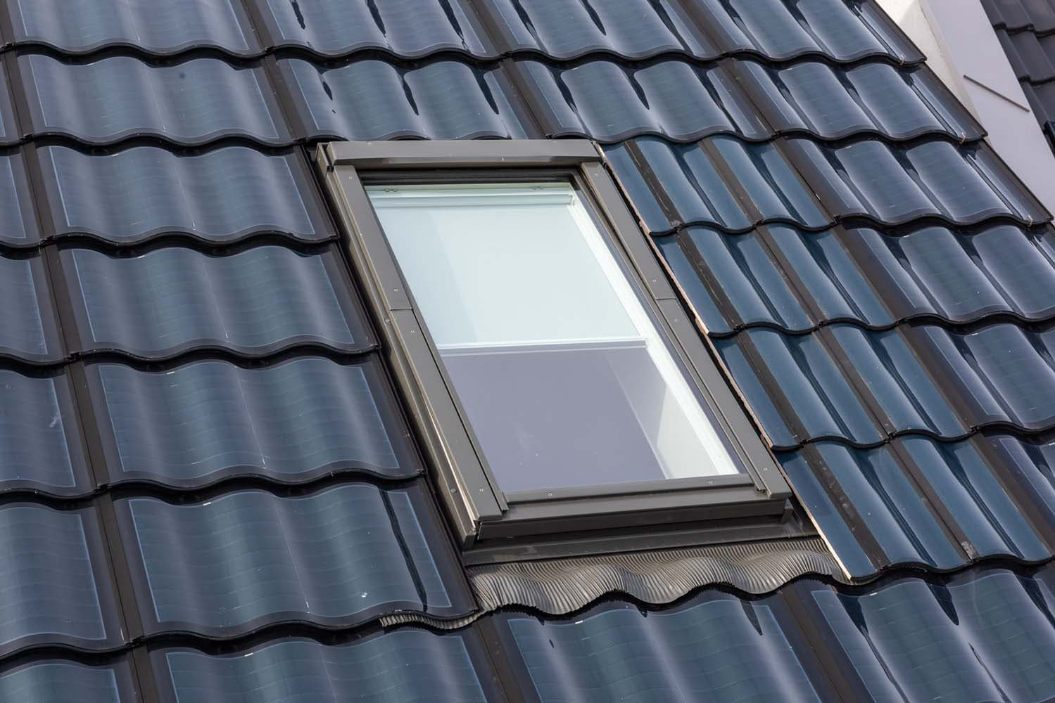 Zwart dak met zonnepanelen die eruit zien als dakpannen en een raam in het midden