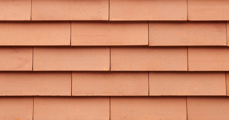 Detail van een oranje getinte muur met grote sidings gevelsysteem Pantheon Nordic die gepotdekseld zijn gemonteerd