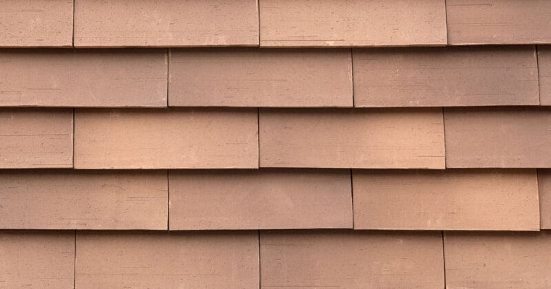 Detail van een bruin/oranje muur met grote sidings gevelsysteem Pantheon Nordic die gepotdekseld zijn gemonteerd