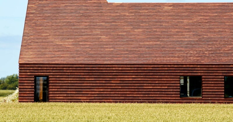 Zijaanzicht van een rood gebouw met ervoor een groen veld