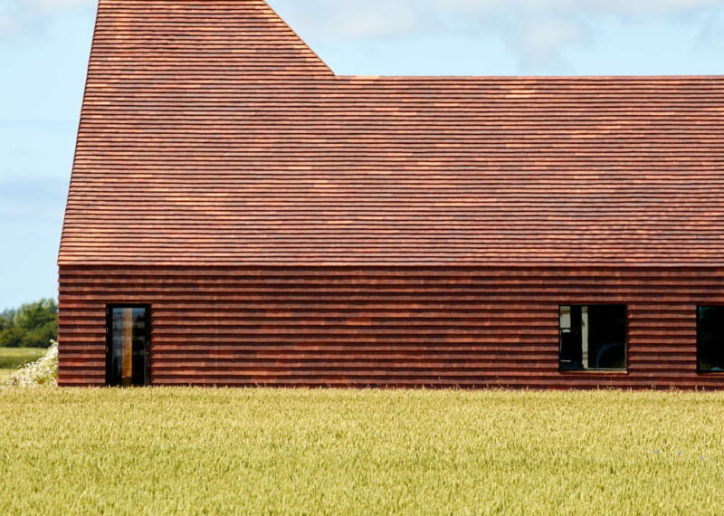 Zijaanzicht van een rood gebouw met ervoor een groen veld