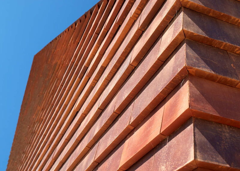 Detail van een rode muur met grote rode sidings tegen een blauwe lucht