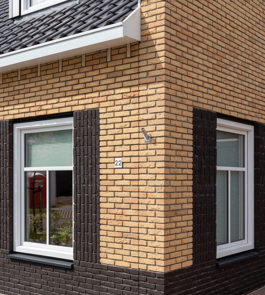Hoek van een huis met lichte bakstenen en donkere dakpannen