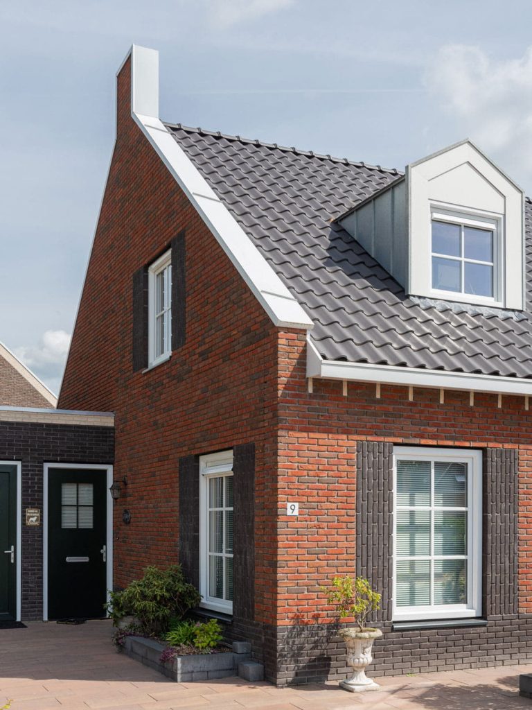 HOek van een huis met roodbruine steen en donkere dakpannen