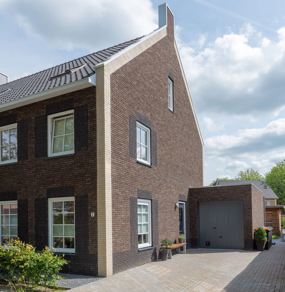 Hoek van een woning met donkere baksteen en een oprit ernast
