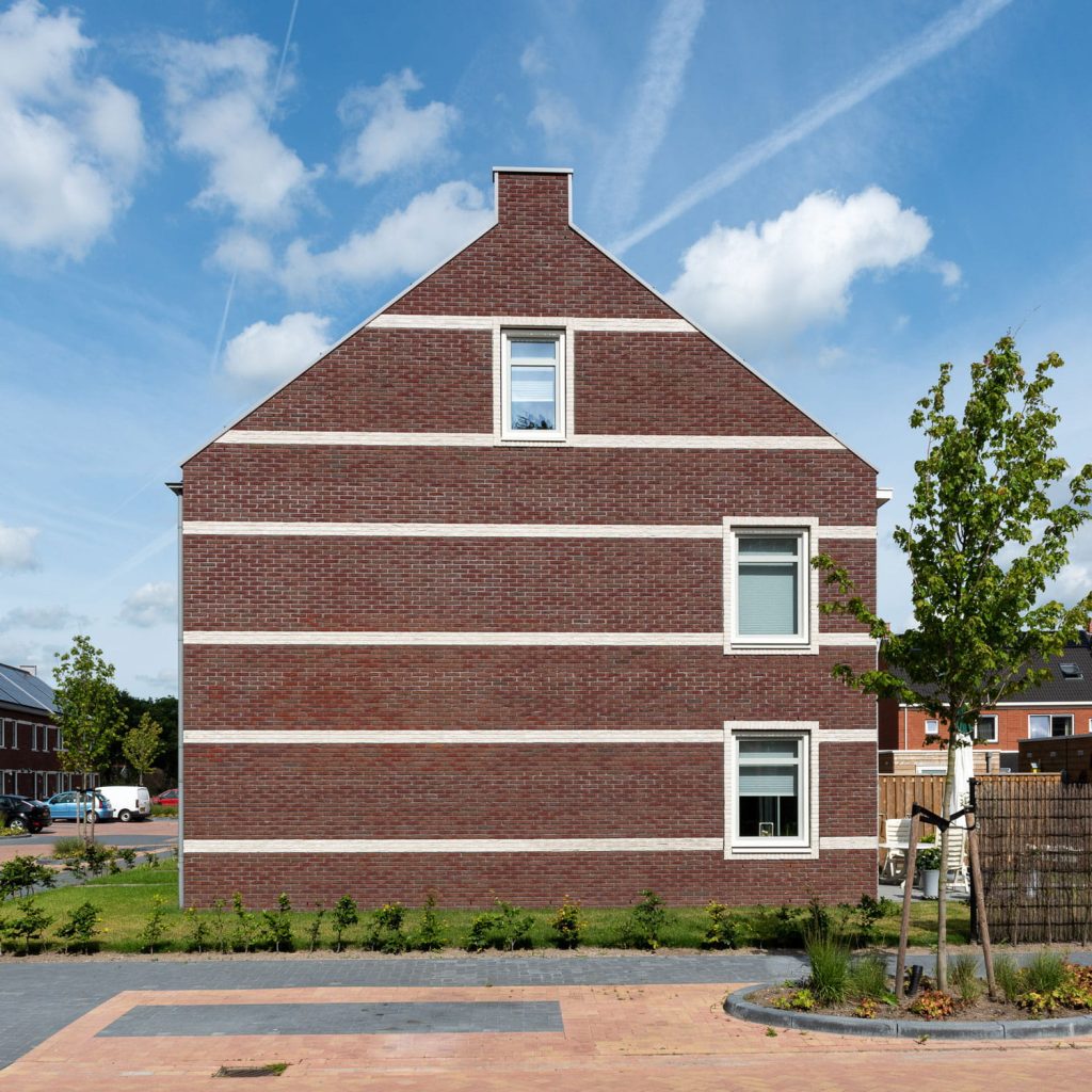 zijkant van een gevel met donkerbruine gevelstenen waar witte lijnen in zitten