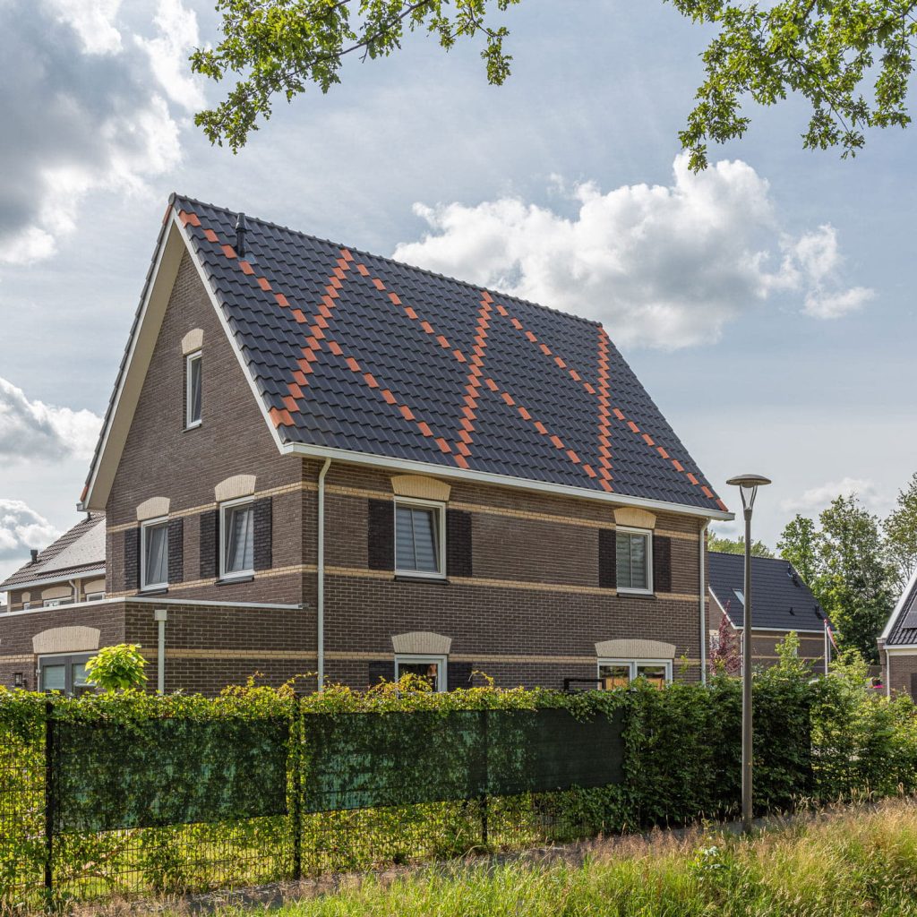 Vrijstaand huis met zwarte dakpannen waarin een kruis van oranje dakpannen zit