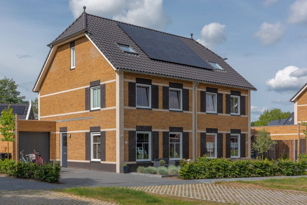 Twee-onder-een-kap met gelige bakstenen en een oprit ervoor, op het dak liggen donkere dagpannen en zonnepanelen