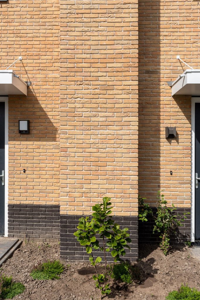 Detail van een muur met gelige gevelstenen en een bruine onderste rand