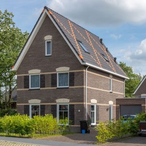 Vrijstaand huis met zwarte dakpannen waarin een kruis van oranje dakpannen zit
