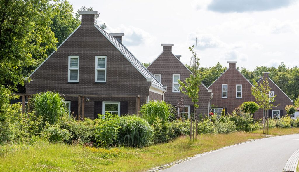 Een aantal woningen achter elkaar in het groen met een donkere baksteen