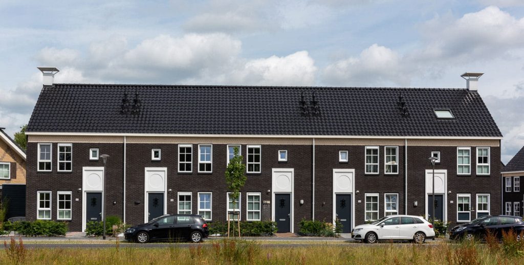 Rijwoning met donkere gevelsteen en witte vlakken en groen ervoor