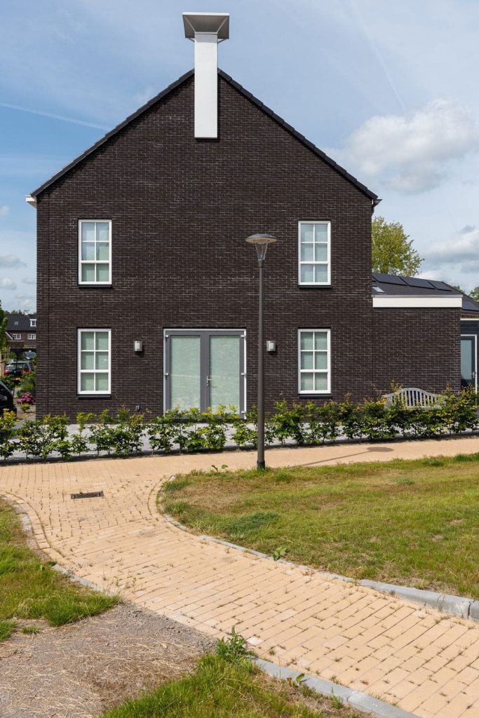 Zijgevel van een huis met donkere gevelsteen en licht pad ervoor