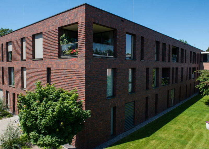 Zijaanzicht van een gebouw met roodbruine gevel en een tuin op de voorgrond