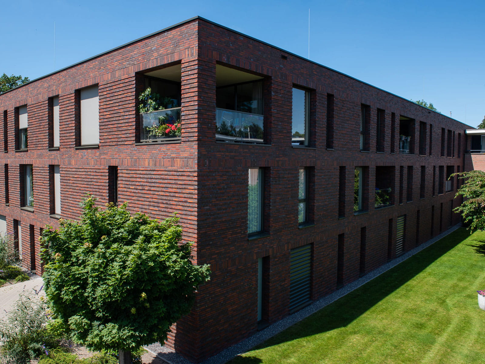 Zijaanzicht van een gebouw met roodbruine gevel en een tuin op de voorgrond