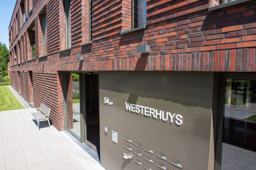 Detail van een muur met roodbruine steenstrips in langformaat en brievenbussen met de tekst Westerhuys