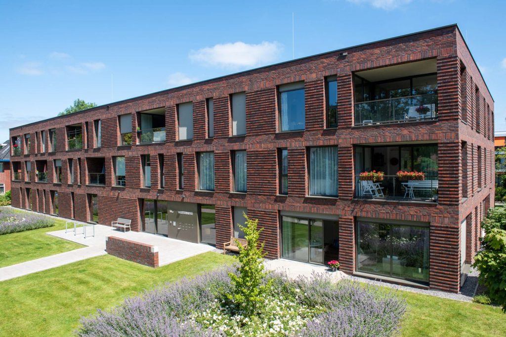 Zijaanzicht van een gebouw met roodbruine steenstrips en een tuin op de voorgrond
