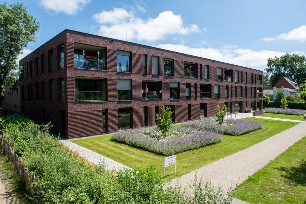 Zijaanzicht van een gebouw met roodbruine steenstrips en een tuin op de voorgrond