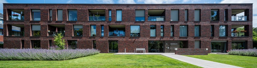 Vooraanzicht van een gebouw met roodbruine steenstrips en een tuin op de voorgrond