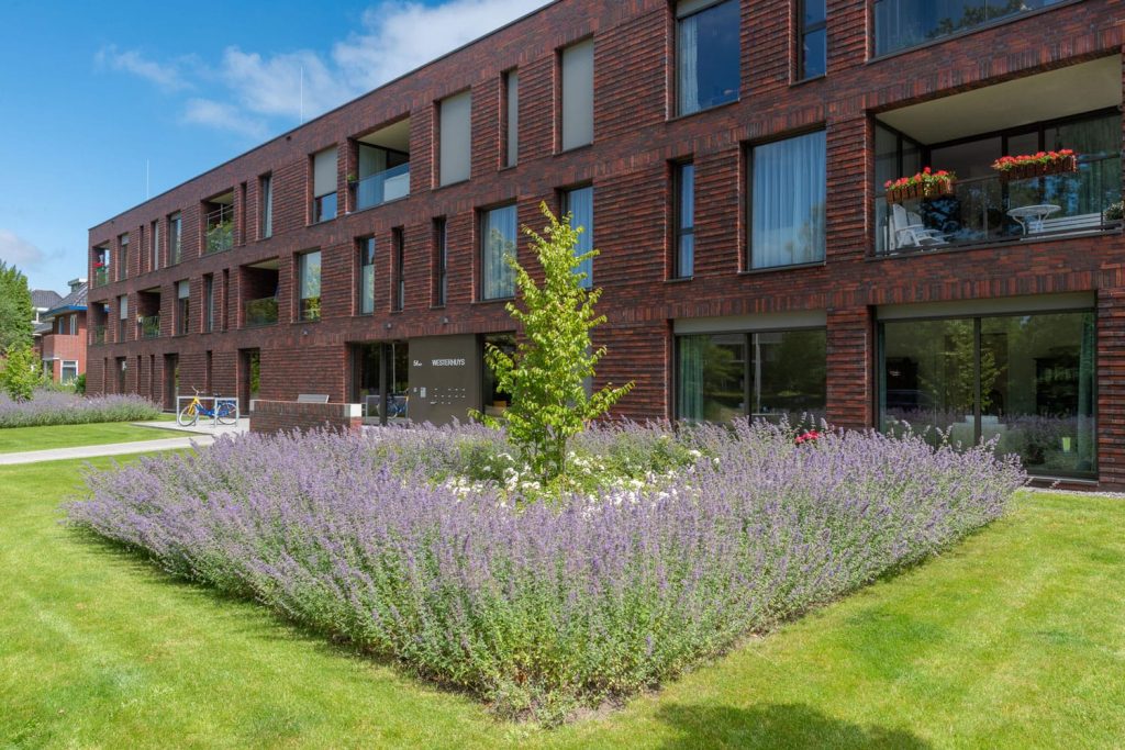 Zijaanzicht van een gebouw met veel ramen en een tuin op de voorgrond