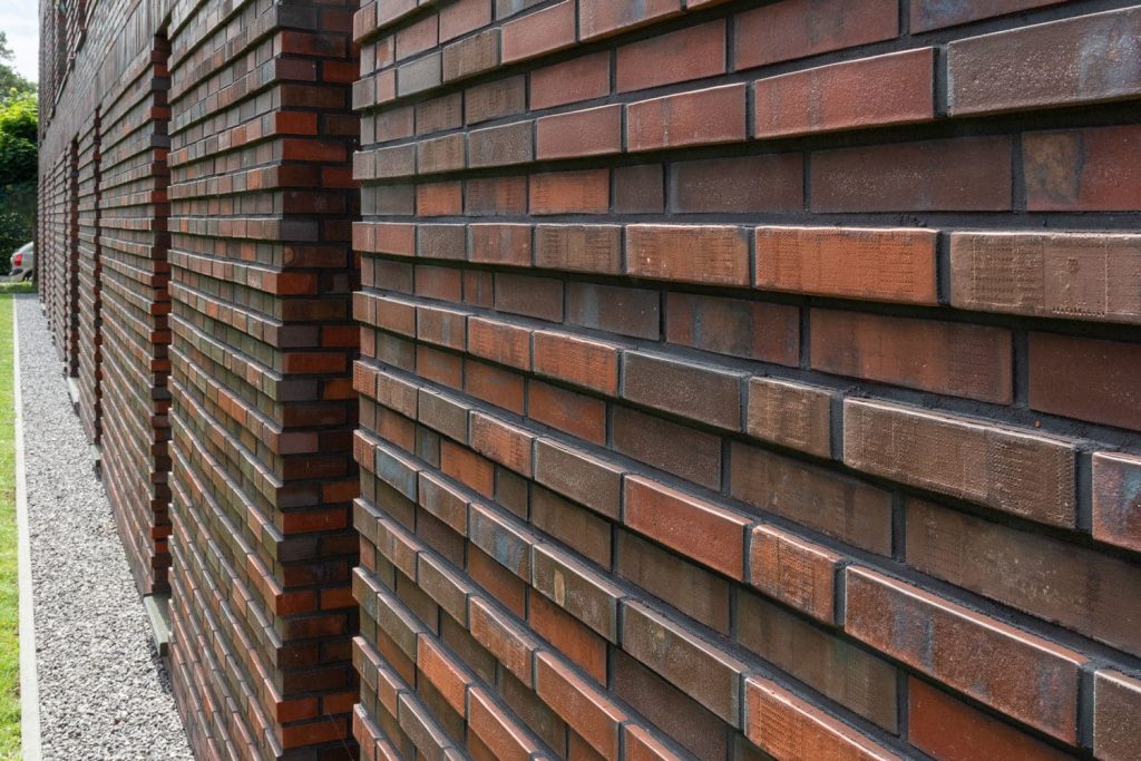 detail van een muur met roodbruine steenstrips in twee diktes