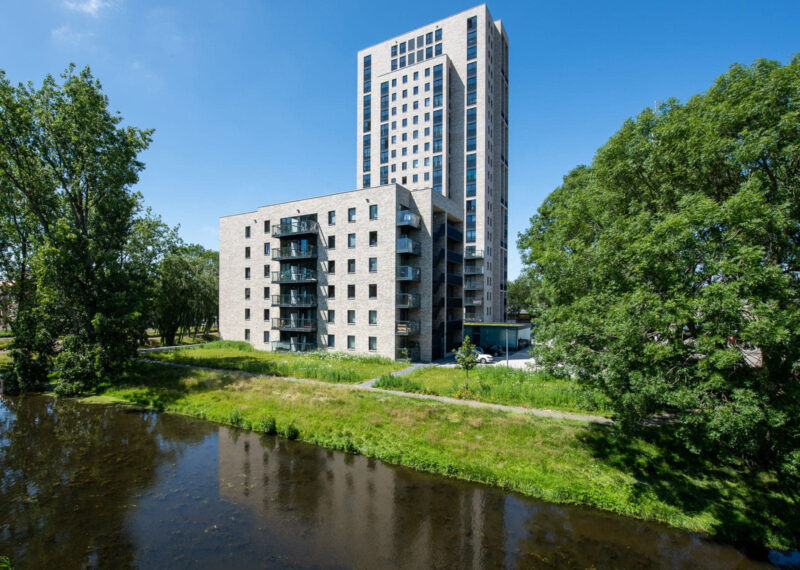 gebouw met lichte gevelstenen en steenstrips met water en groen op de voorgrond